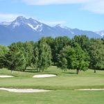 Panoramic view of a lush green golf course at Mission Mountain Golf Club. Smooth